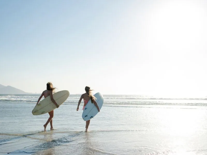 Couple walking the beach with boards at sunset