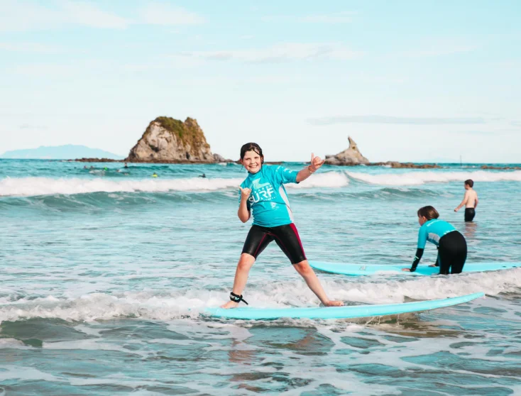 Grom celebrating a ride at Mangawhai Heads with the rock stacks behind