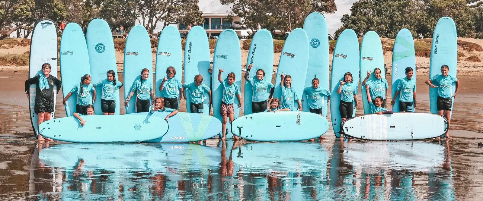 School group lined up with soft boards on the beach