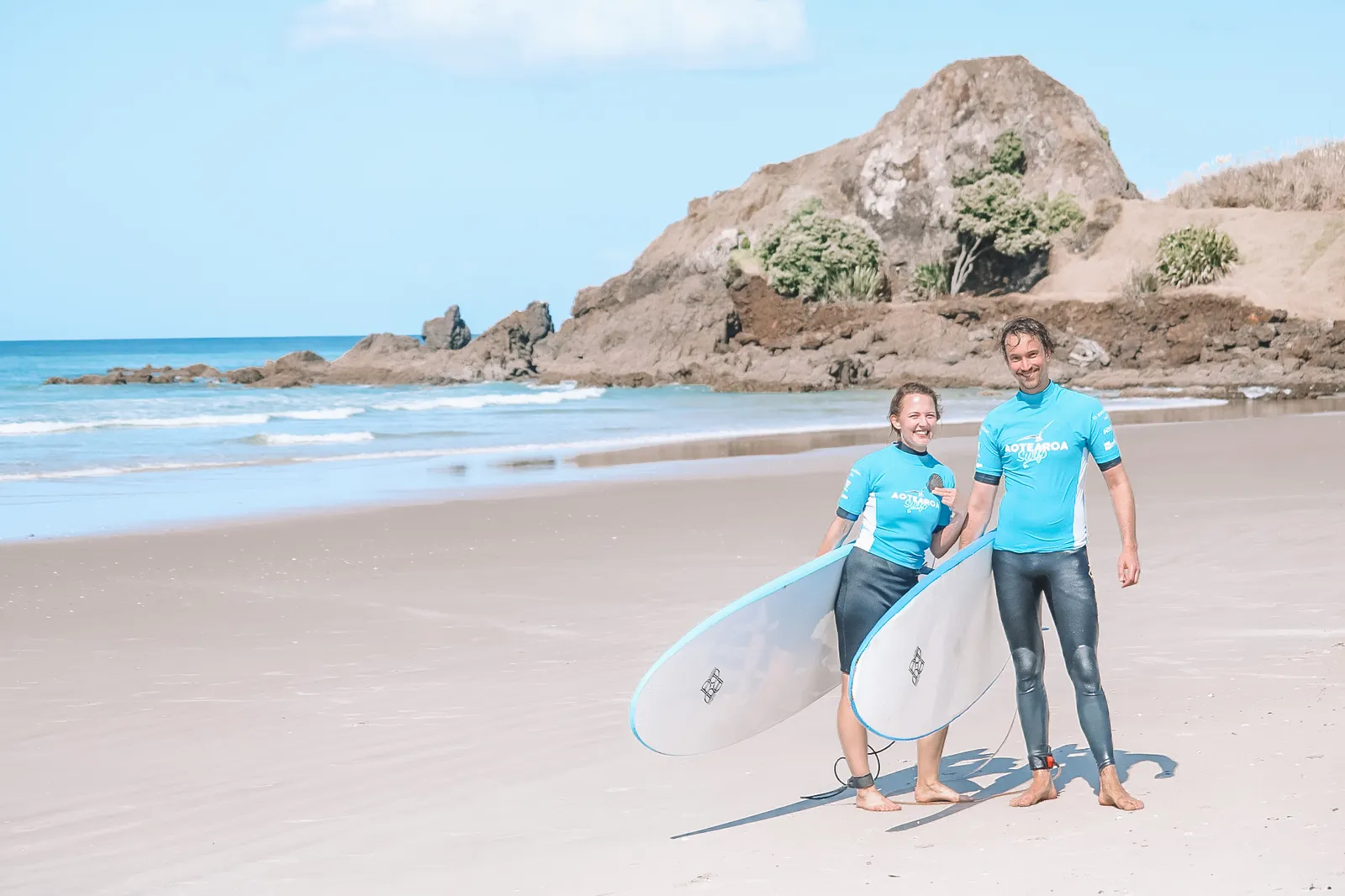 Two learners carrying soft boards up the beach after a lesson