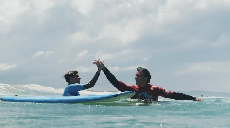 Teens high fiving in the water at youth surf camp