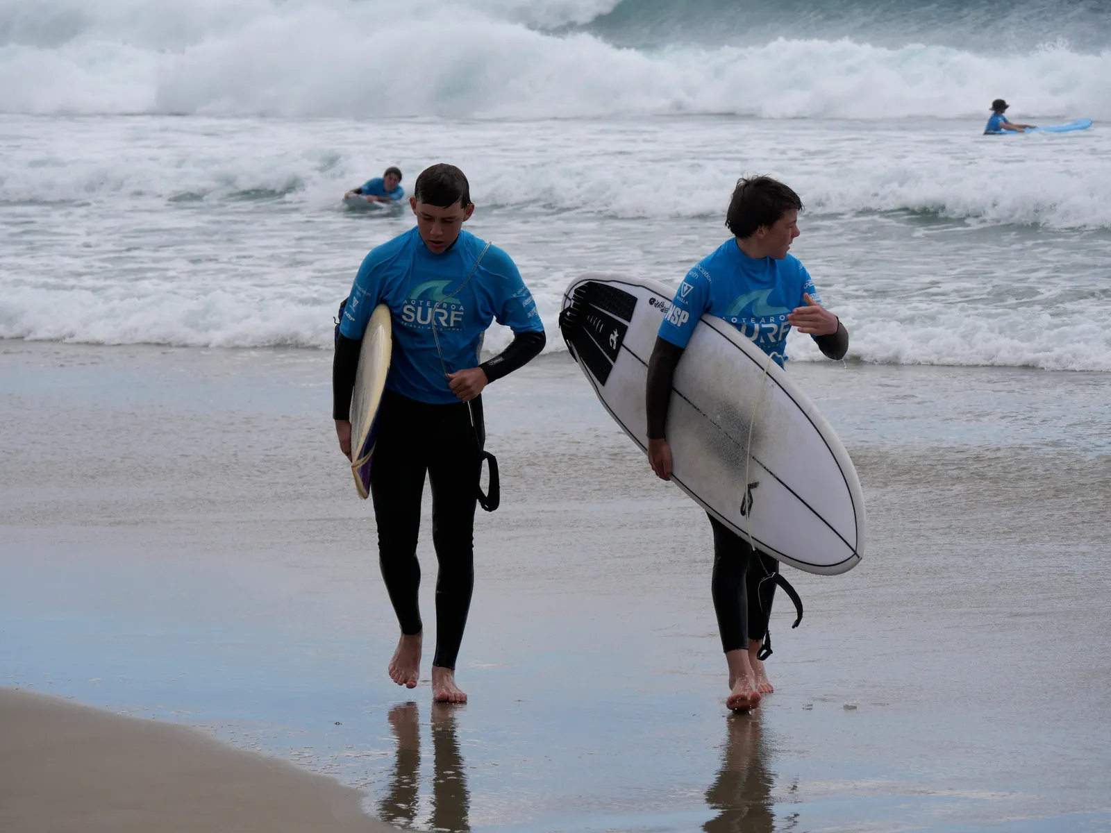 Teens walking out to the surf with boards under arm